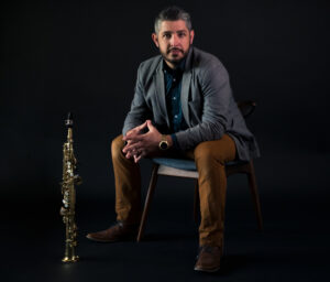 Mathew Younglove seated with a soprano saxophone on his right